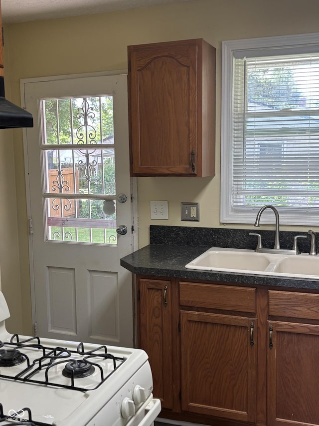 3031 W 18th St, Indianapolis, IN 46222 - kitchen featuring white range with gas cooktop, a sink, dark countertops, brown cabinetry, and extractor fan