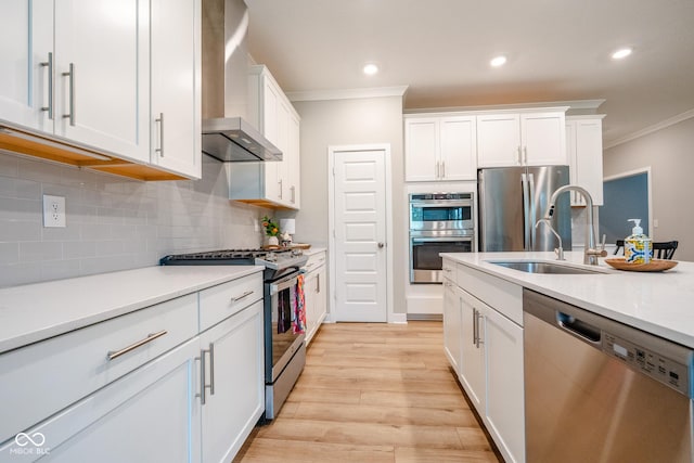 9741 Haughton Ln, Mccordsville, IN 46055 - kitchen with stainless steel appliances, wall chimney range hood, ornamental molding, white cabinetry, and light wood finished floors