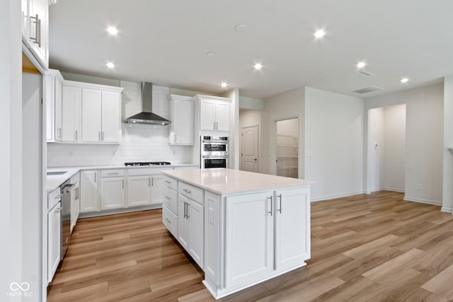 7248 Covington St, Lebanon, IN 46052 - kitchen featuring wall chimney range hood, appliances with stainless steel finishes, a kitchen island, tasteful backsplash, and light wood-style flooring