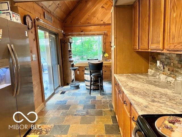 6774 S Becks Grove Rd, Freetown, IN 47235 - kitchen featuring stainless steel fridge with ice dispenser, vaulted ceiling, healthy amount of natural light, brown cabinets, and stone finish flooring