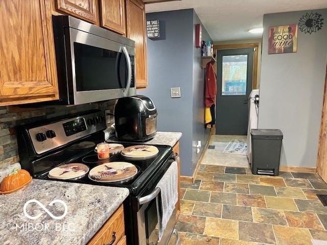 6774 S Becks Grove Rd, Freetown, IN 47235 - kitchen featuring stainless steel appliances, baseboards, stone finish flooring, and brown cabinetry