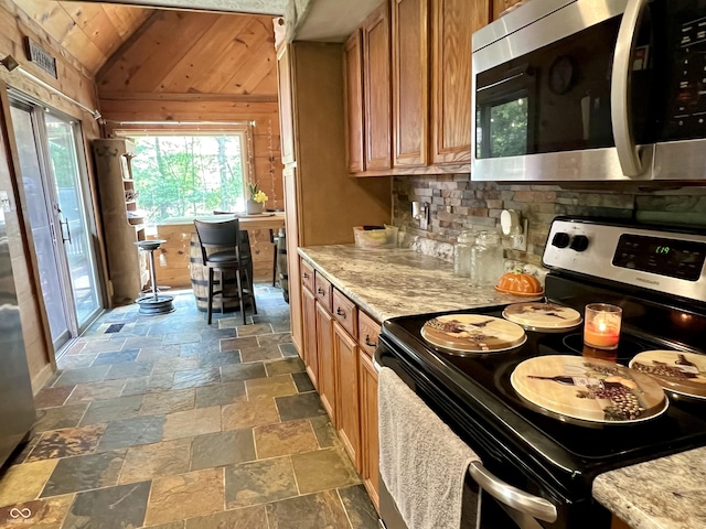 6774 S Becks Grove Rd, Freetown, IN 47235 - kitchen featuring appliances with stainless steel finishes, stone tile flooring, brown cabinets, vaulted ceiling, and tasteful backsplash