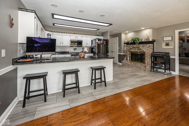 28 Patriot Ct, Greenfield, IN 46140 - kitchen featuring stainless steel microwave, a peninsula, freestanding refrigerator, backsplash, and white cabinetry