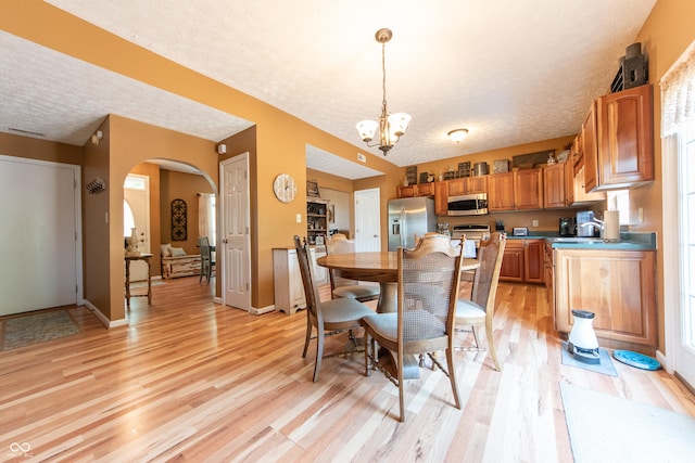 977 Canary Creek Dr, Franklin, IN 46131 - dining room with light wood-type flooring, a chandelier, arched walkways, and a textured ceiling