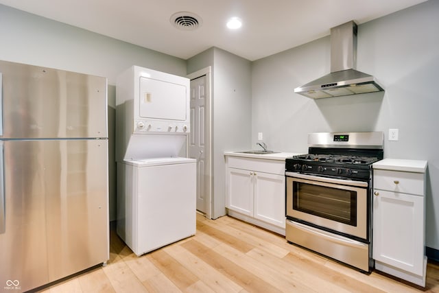 5002 E Washington St, Indianapolis, IN 46201 - kitchen featuring wall chimney range hood, stainless steel appliances, estacked washer and dryer, light wood-style floors, and white cabinetry