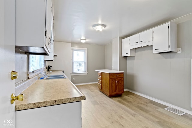 1021 W 37th St, Indianapolis, IN 46208 - kitchen with light wood-type flooring, white cabinetry, a sink, light countertops, and baseboards