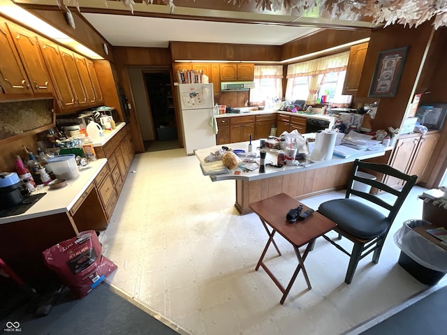 851 E Franklin St, Spencer, IN 47460 - kitchen featuring freestanding refrigerator, light flooring, a peninsula, brown cabinetry, and wood walls
