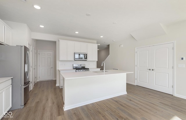 9741 Oleander Dr, Fishers, IN 46250 - kitchen featuring appliances with stainless steel finishes, a sink, light wood finished floors, decorative backsplash, and a center island with sink
