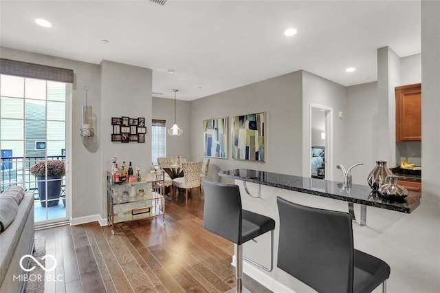 435 Virginia Ave Unit 108, Indianapolis, IN 46203 - kitchen with a kitchen bar, dark wood-type flooring, brown cabinetry, dark stone countertops, and recessed lighting