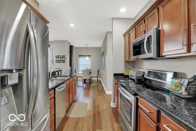 435 Virginia Ave Unit 108, Indianapolis, IN 46203 - kitchen with stainless steel appliances, a sink, light wood finished floors, brown cabinetry, and dark stone counters