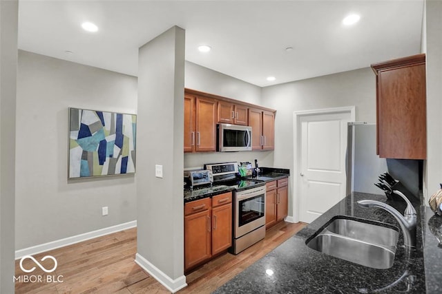 435 Virginia Ave Unit 108, Indianapolis, IN 46203 - kitchen featuring appliances with stainless steel finishes, a sink, light wood-style flooring, dark stone countertops, and baseboards