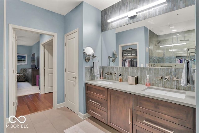 435 Virginia Ave Unit 108, Indianapolis, IN 46203 - bathroom featuring a stall shower, double vanity, tasteful backsplash, a spacious closet, and tile patterned floors