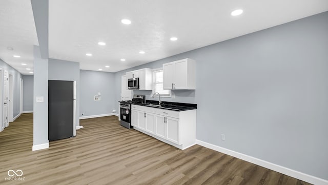 3106 N Harding St, Indianapolis, IN 46208 - kitchen with stainless steel appliances, a sink, baseboards, light wood finished floors, and white cabinets