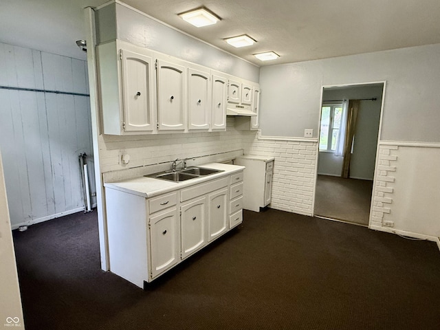 3325 Canaday Dr, Anderson, IN 46013 - kitchen with dark colored carpet, white cabinetry, a sink, light countertops, and wooden walls