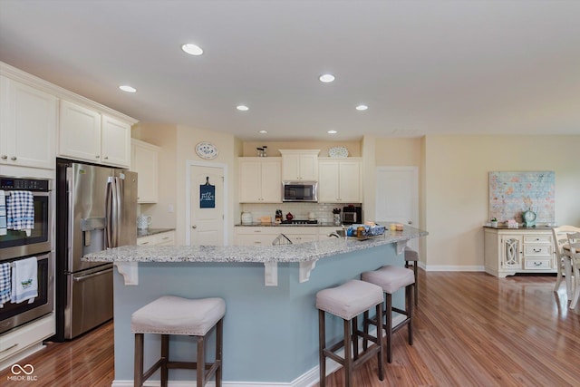6337 Ederline Ln, Noblesville, IN 46062 - kitchen featuring stainless steel appliances, wood finished floors, tasteful backsplash, a kitchen bar, and white cabinetry