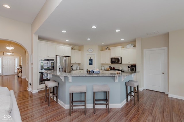 6337 Ederline Ln, Noblesville, IN 46062 - kitchen with stainless steel appliances, arched walkways, light wood-style flooring, a kitchen bar, and recessed lighting