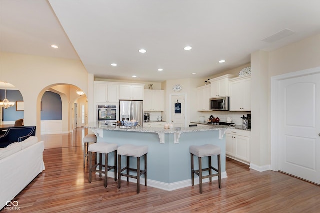 6337 Ederline Ln, Noblesville, IN 46062 - kitchen featuring appliances with stainless steel finishes, arched walkways, a kitchen breakfast bar, light wood-style floors, and recessed lighting