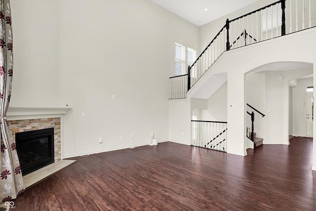 7046 Allegiance Ct, Indianapolis, IN 46259 - unfurnished living room with wood finished floors, a towering ceiling, arched walkways, stairway, and a stone fireplace