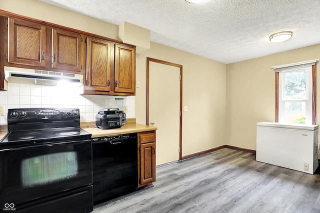 926 Brookside Ln, Plainfield, IN 46168 - kitchen with black appliances, under cabinet range hood, light wood-style flooring, decorative backsplash, and light countertops