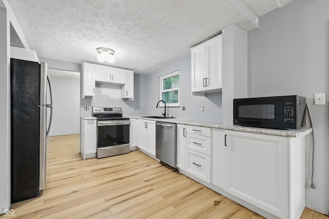 1826 Shorter Dr, Indianapolis, IN 46214 - kitchen with stainless steel appliances, a sink, light wood-style floors, white cabinets, and a textured ceiling