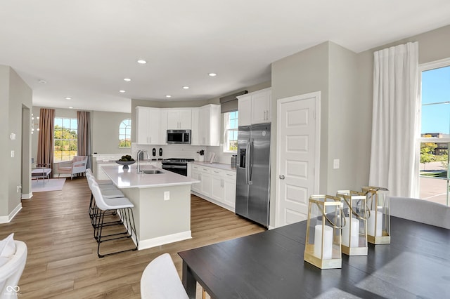 6702 Halsey St, Zionsville, IN 46077 - kitchen with appliances with stainless steel finishes, a sink, an island with sink, decorative backsplash, and light wood-style floors
