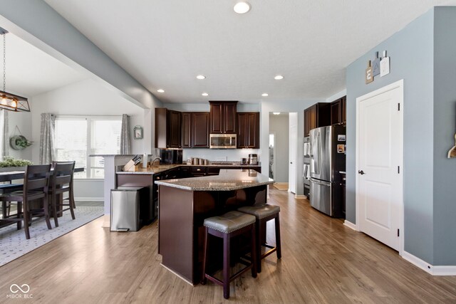13485 Mancroft Dr, Fishers, IN 46037 - kitchen with stainless steel appliances, a kitchen island, a kitchen bar, dark brown cabinetry, and light wood-type flooring
