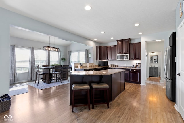 13485 Mancroft Dr, Fishers, IN 46037 - kitchen with stainless steel appliances, dark brown cabinetry, a kitchen breakfast bar, light wood-type flooring, and recessed lighting