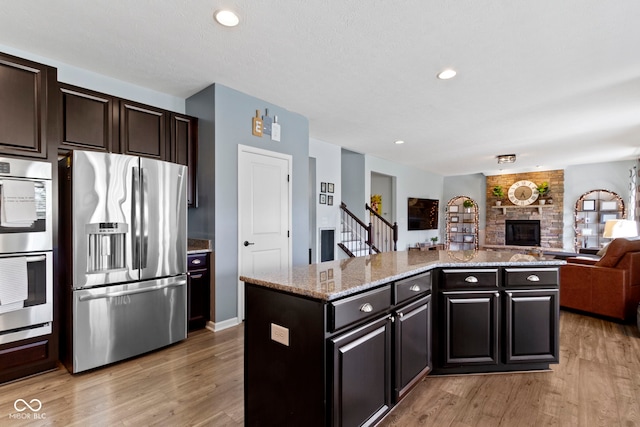13485 Mancroft Dr, Fishers, IN 46037 - kitchen with stainless steel appliances, open floor plan, light wood-style floors, a large fireplace, and a center island