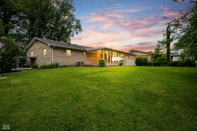 7482 W US Highway 40, Indianapolis, IN 46229 - back of house at dusk with stone siding, a chimney, a yard, and central AC