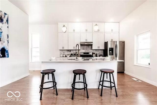 918 S State Ave, Indianapolis, IN 46203 - kitchen with a kitchen bar, light wood-type flooring, decorative backsplash, white cabinets, and an island with sink