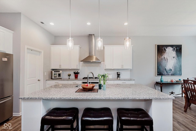 15593 Marsden Dr, Westfield, IN 46074 - kitchen with freestanding refrigerator, wall chimney range hood, wood finished floors, white cabinets, and a kitchen island with sink