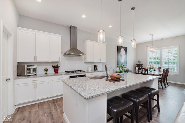 15593 Marsden Dr, Westfield, IN 46074 - kitchen featuring wall chimney range hood, light wood-style flooring, white cabinets, a center island with sink, and recessed lighting