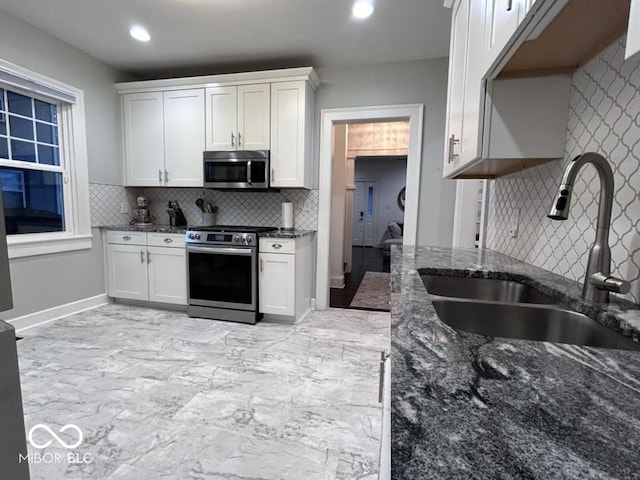 4040 Carrollton Ave, Indianapolis, IN 46205 - kitchen with appliances with stainless steel finishes, a sink, decorative backsplash, light marble finish flooring, and white cabinetry