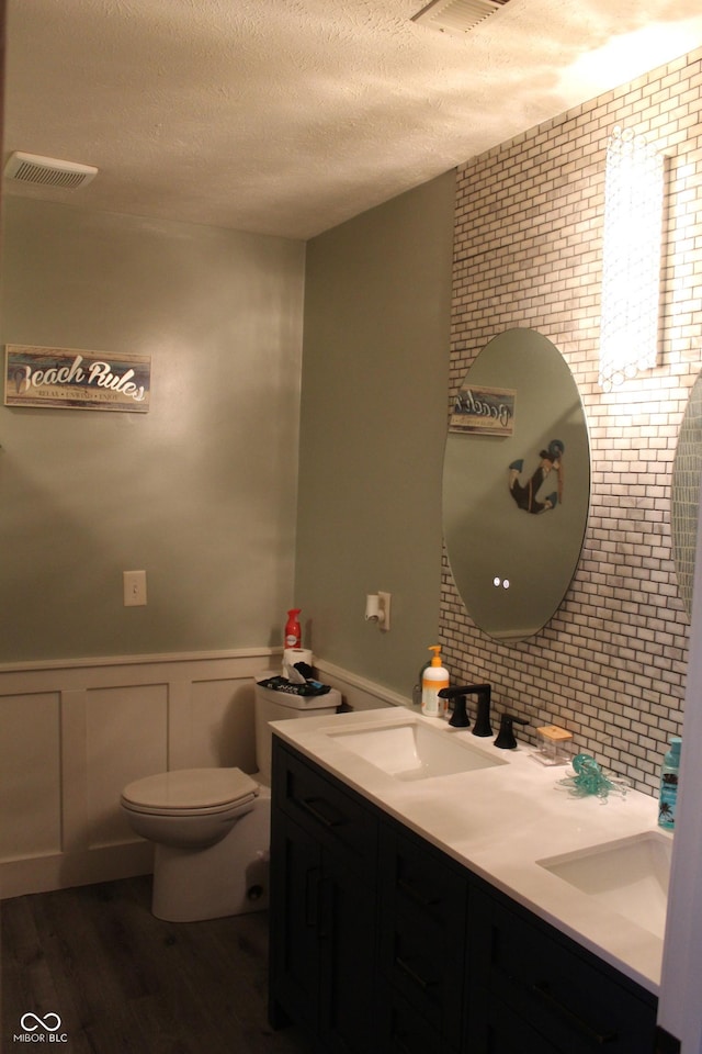 5101 W Bay Rd, Plainfield, IN 46168 - bathroom with double vanity, a textured ceiling, wood finished floors, toilet, and wainscoting
