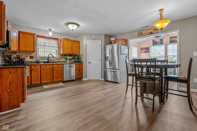 2730 Foxbriar Pl, Indianapolis, IN 46203 - kitchen featuring appliances with stainless steel finishes, brown cabinets, light wood finished floors, decorative backsplash, and a textured ceiling