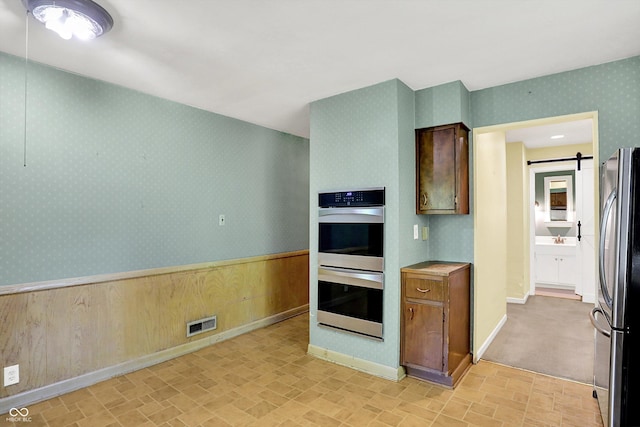 3215 E Edgewood Ave, Indianapolis, IN 46227 - kitchen featuring stainless steel appliances, wallpapered walls, a barn door, baseboards, and light countertops