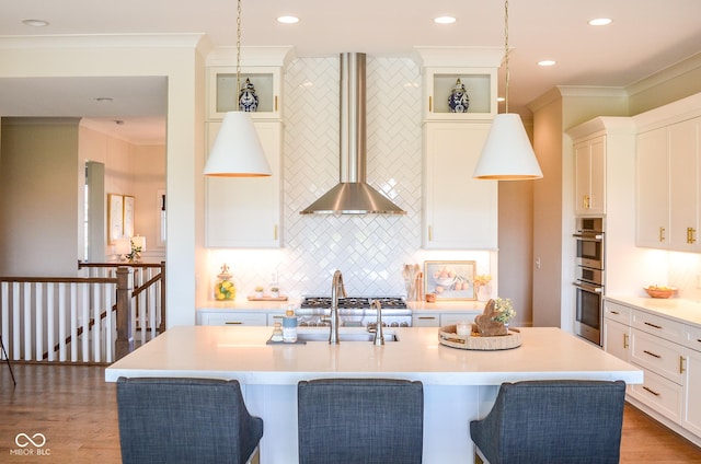 987 Oak Terrace Rd, Westfield, IN 46074 - kitchen with wall chimney exhaust hood, light countertops, white cabinetry, an island with sink, and backsplash