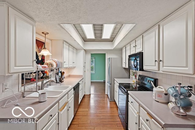 813 Boulder Rd, Indianapolis, IN 46217 - kitchen featuring black appliances, light wood-style flooring, white cabinetry, a sink, and a tray ceiling