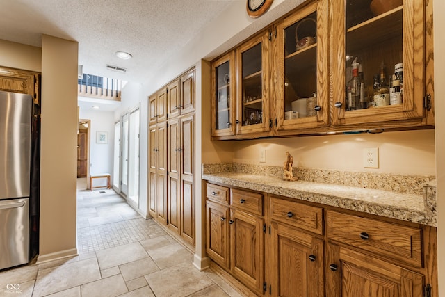 5326 White Marsh Ln, Indianapolis, IN 46226 - kitchen featuring freestanding refrigerator, brown cabinetry, glass insert cabinets, baseboards, and a textured ceiling
