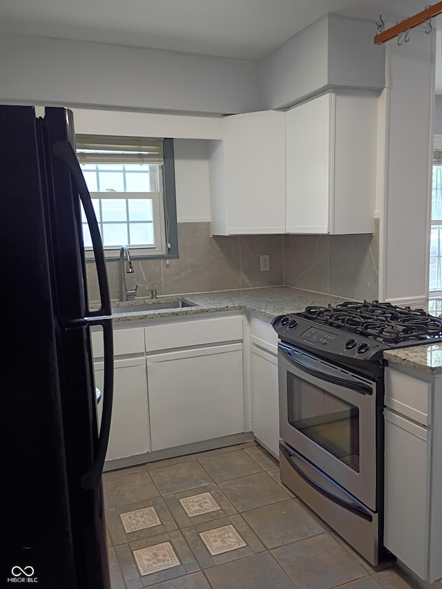 1008 E 61st St, Indianapolis, IN 46220 - kitchen with freestanding refrigerator, stainless steel gas stove, white cabinetry, tasteful backsplash, and a sink