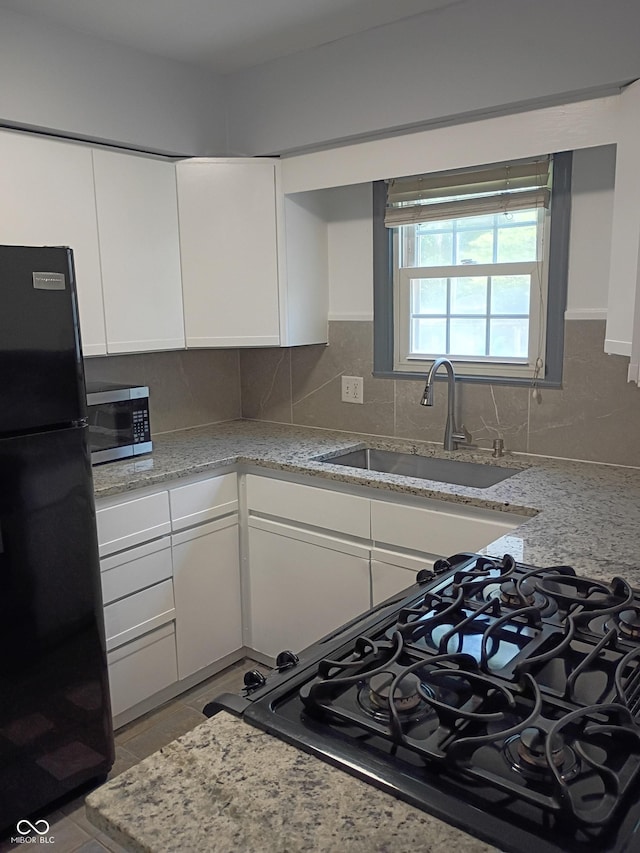 1008 E 61st St, Indianapolis, IN 46220 - kitchen with freestanding refrigerator, stainless steel microwave, a sink, white cabinets, and backsplash