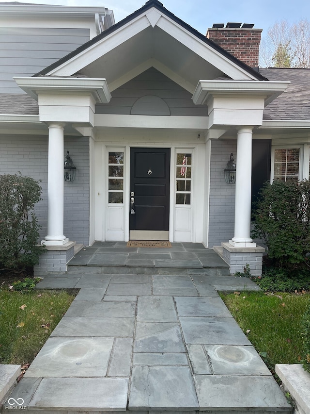 9510 Copley Dr, Indianapolis, IN 46260 - view of exterior entry featuring brick siding, covered porch, a chimney, and roof with shingles