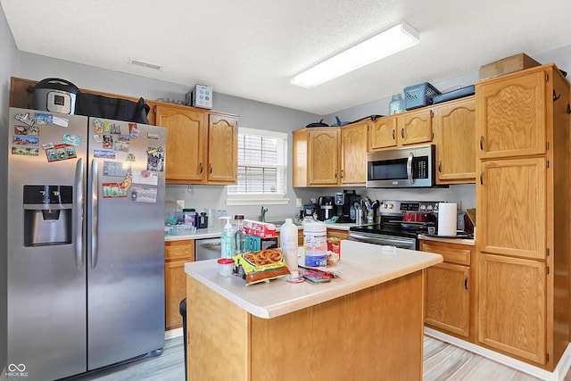 15264 Ten Point Dr, Noblesville, IN 46060 - kitchen featuring stainless steel appliances, light countertops, light wood-type flooring, a center island, and a textured ceiling