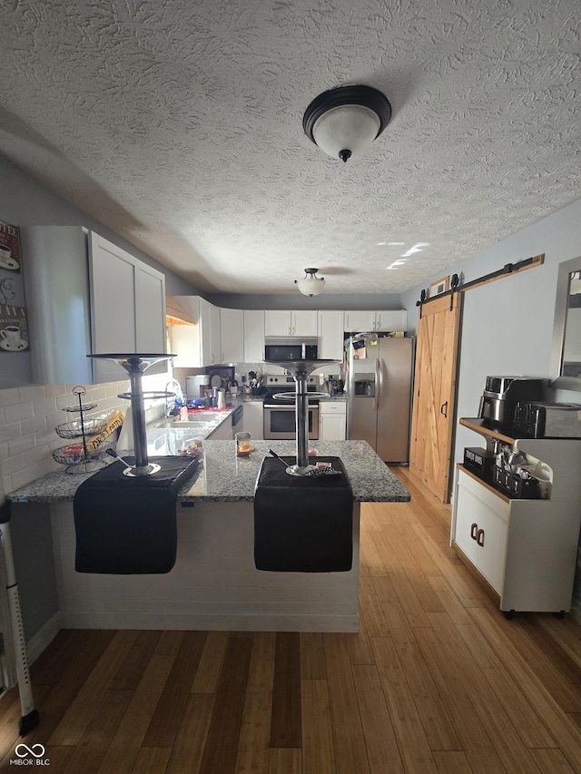 2248 Salem Park Dr, Indianapolis, IN 46239 - kitchen featuring stainless steel appliances, a peninsula, a barn door, white cabinetry, and light wood-style flooring