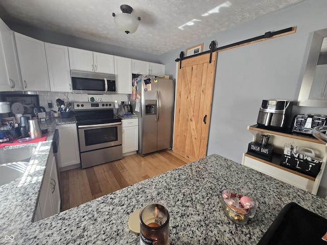 2248 Salem Park Dr, Indianapolis, IN 46239 - kitchen with appliances with stainless steel finishes, a barn door, light wood-style flooring, light stone counters, and a textured ceiling