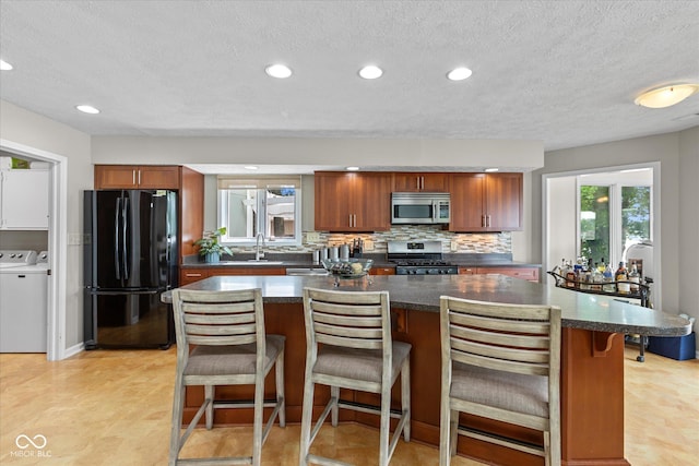 101 Edgewater Dr, Noblesville, IN 46062 - kitchen with stainless steel appliances, dark countertops, backsplash, washing machine and dryer, and a textured ceiling