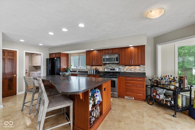 101 Edgewater Dr, Noblesville, IN 46062 - kitchen with stainless steel appliances, dark countertops, washing machine and clothes dryer, a breakfast bar, and a center island