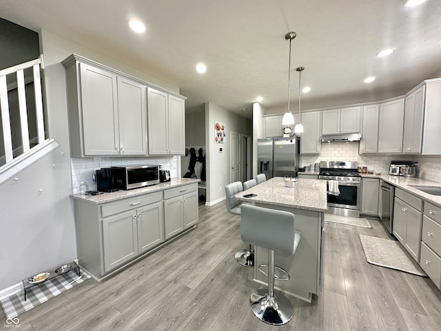 9133 Thames Dr, Avon, IN 46123 - kitchen with appliances with stainless steel finishes, under cabinet range hood, gray cabinetry, backsplash, and light wood-style floors
