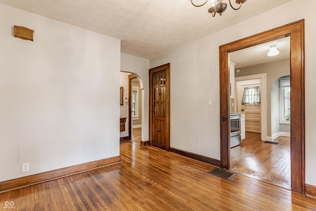 595 W Poplar St, Zionsville, IN 46077 - empty room featuring arched walkways, hardwood / wood-style flooring, baseboards, a textured ceiling, and a chandelier