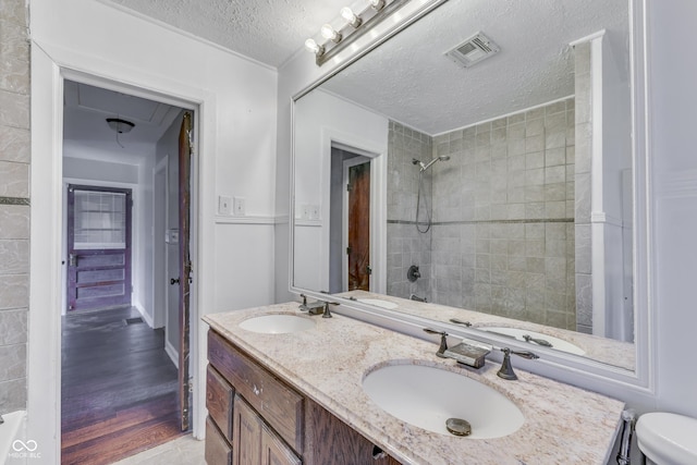 1601 Southern Ave, Beech Grove, IN 46107 - bathroom with a textured ceiling, a tile shower, double vanity, toilet, and wood finished floors